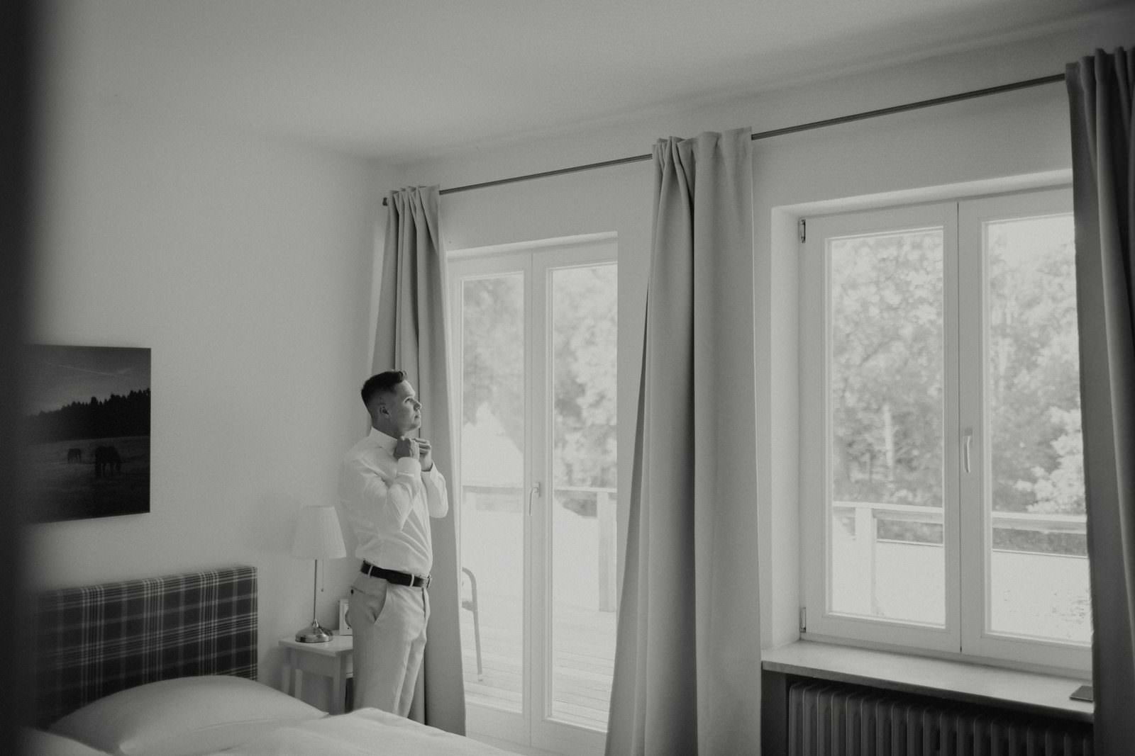 Basti am Fenster: Krawatte binden, Schwarzweiß, Hotelzimmer mit Ausblick in den Park.
