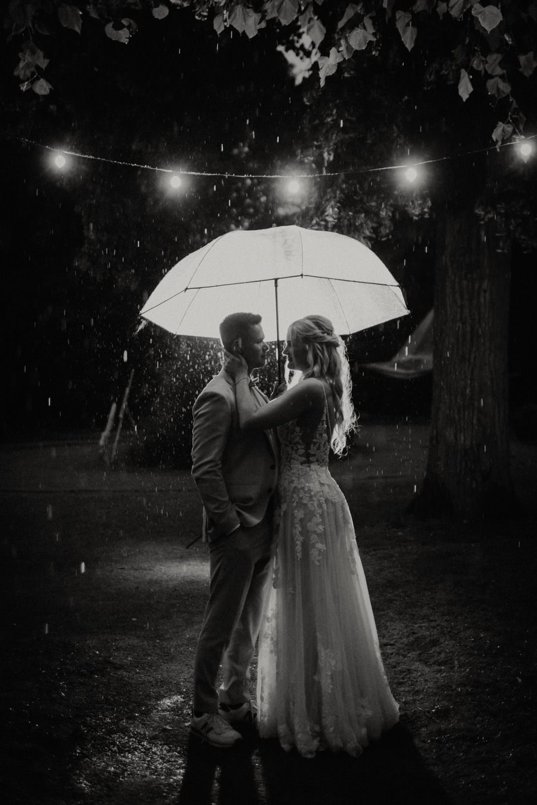 Regenshooting in der blauen Stunde: Cyana und Basti unter transparentem Schirm, Lichterkette, sichtbarer Regen.
